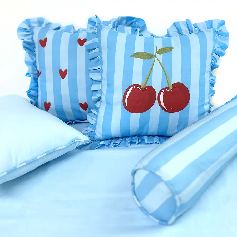 Conjunto de almofadas listradas de azul com desenho de cereja e de corações, além de rolo listrado
